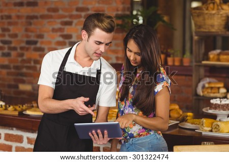 Waiter and pretty customer pointing on tablet computer at coffee shop