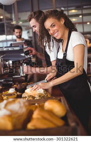 Portrait of smiling waitress cutting bread in front of colleague at coffee shop