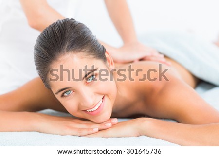 Pretty brunette enjoying a massage smiling at camera at the health spa