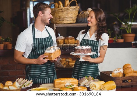 Smiling co-workers showing bread and cake at the coffee shop