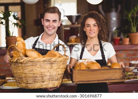 Portrait of smiling waiter and waitress holding basket full of bread rolls at coffee shop