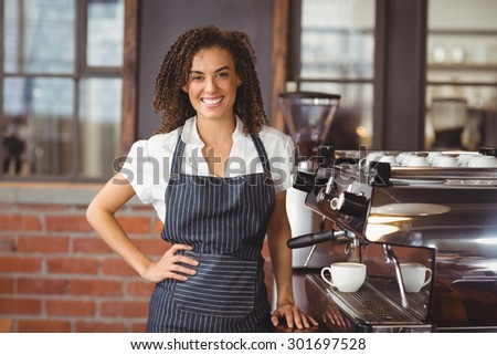 Portrait of pretty barista smiling next to coffee machine at coffee shop