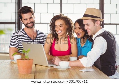 Smiling friends looking at laptop and having coffee at coffee shop