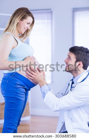Smiling doctor checking stomach of standing pregnant patient in medical office