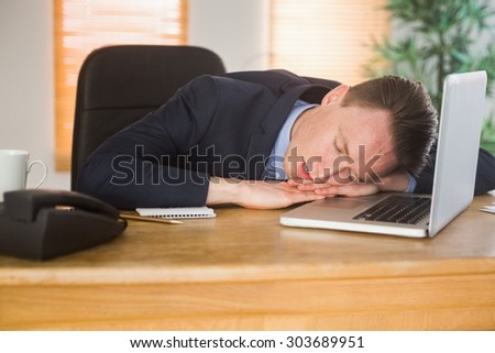 Exhausted businessman sleeping on his laptop in the office
