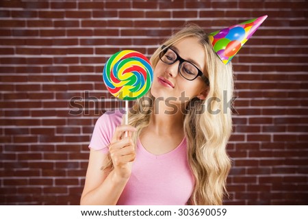 A beautiful hipster with party hat holding a giant lollipop against a red brick