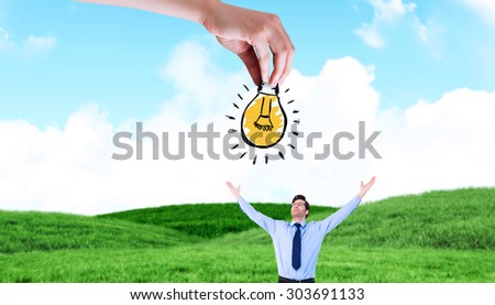 Hand holding light bulb doodle against blue sky over grass