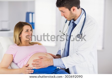 Doctor examining stomach of pregnant patient and giving advice in medical office