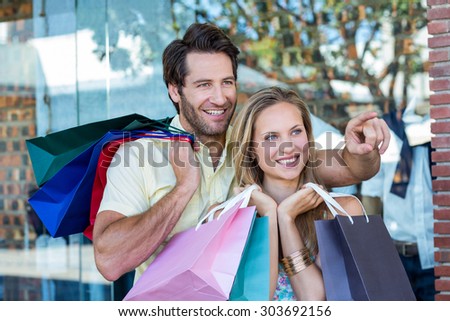 Smiling couple with shopping bags looking and pointing at shopping mall
