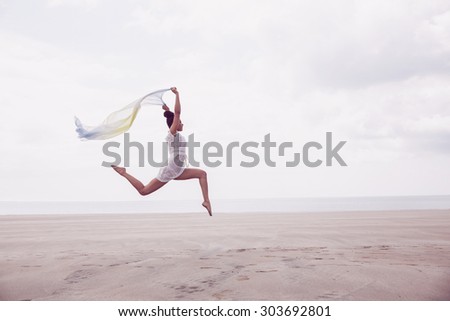 Stylish woman leaping with scarf at the beach