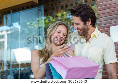 Laughing couple using smartphone at shopping mall