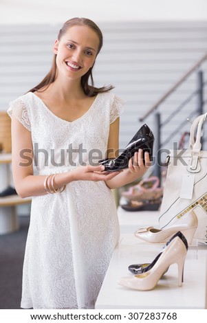Pretty brunette smiling at camera and showing a heel shoe in shoe store