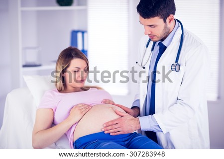 Doctor checking stomach of pregnant patient in medical office