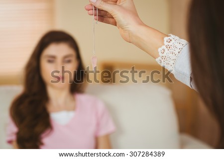 Hypnotherapist holding pendulum before her patient in therapists office