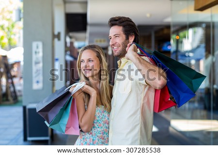 Smiling couple with shopping bags looking far away at shopping mall