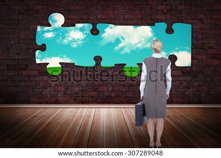 Back turned businesswoman holding a briefcase against green field under blue sky