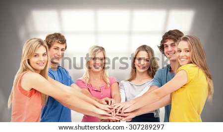 Friends standing around each other as they stack their hands against room with large window showing city