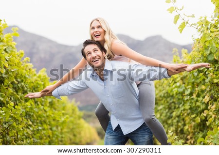 Young happy man carrying happy woman on his back in the grape fields