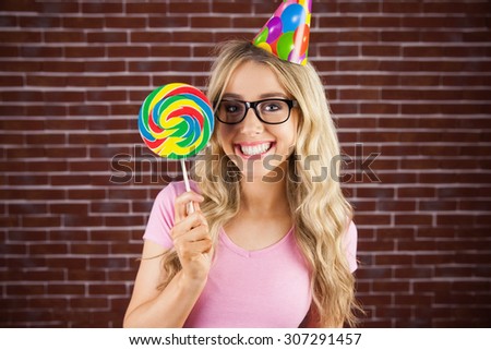 Portrait of a hipster with a party hat holding a lollipop against a red brick wall