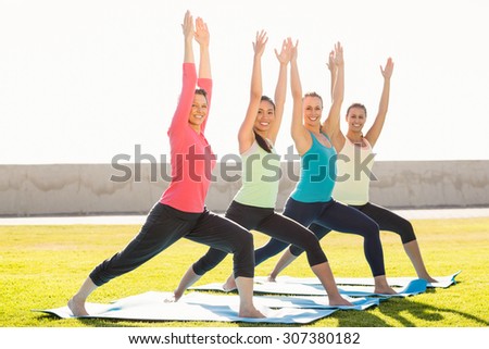 Portrait of smiling sporty women doing warrior pose in yoga class in parkland
