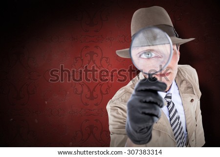 Spy looking through magnifier against elegant patterned wallpaper in red tones