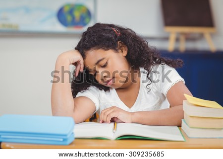 Concentrated pupil reading notepad in a classroom in school