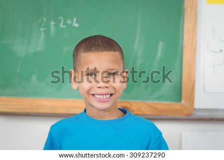 Portrait of cute pupil standing in front of chalkboard in a classroom