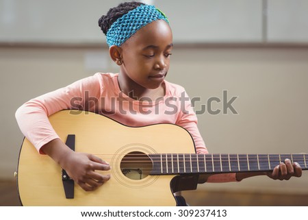 Focused pupil playing guitar in a classroom in school