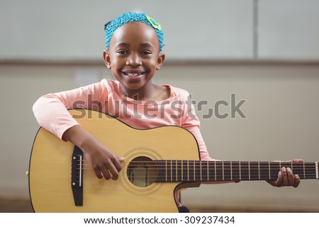 Portrait of smiling pupil playing guitar in a classroom in school