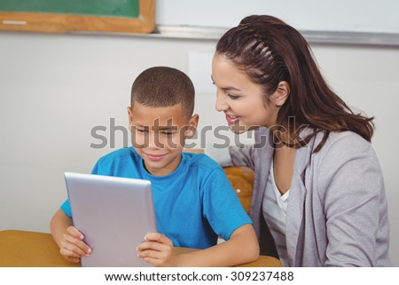 Pretty teacher and pupil using tablet at his desk in a classroom