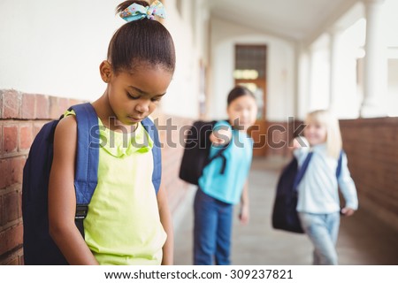 Sad pupil being bullied by classmates at corridor in school