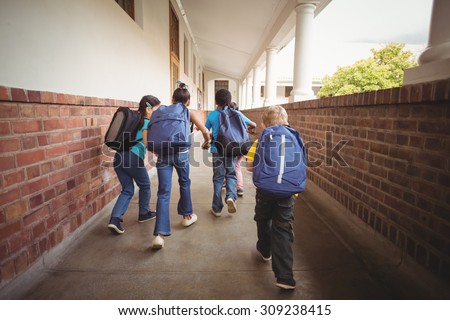 Rear view of pupils walking at corridor in school