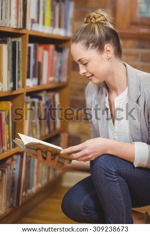 Blonde teacher searching book in the library in school