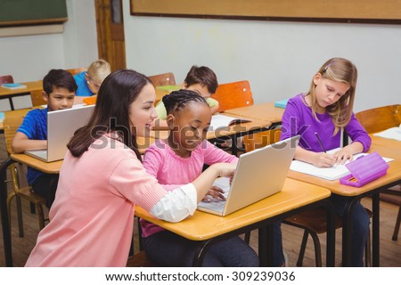 Happy teacher using laptop with student at the elementary school