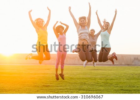 Portrait of happy sporty women jumping during fitness class in parkland