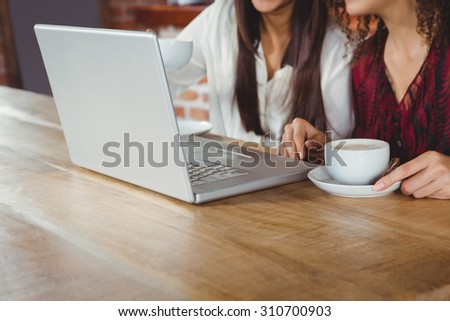Happy women friends drinking coffee and looking at laptop outside at a cafe
