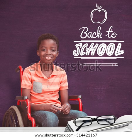 Full length portrait of happy boy on wheelchair against green chalkboard