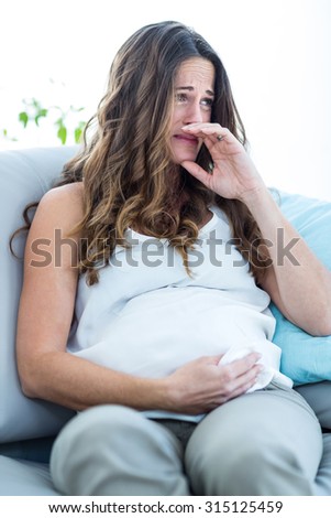 Pregnant woman crying while sitting on sofa at home