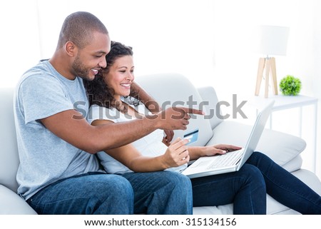 Couple enjoying online shopping sitting on sofa at home