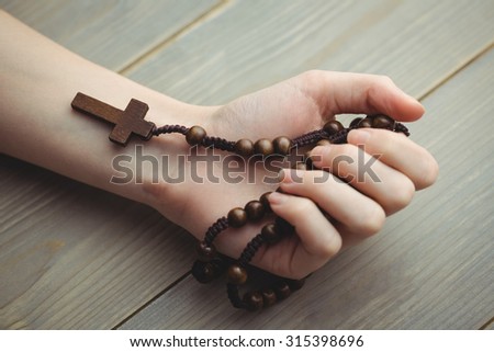 Woman holding wooden rosary beads on table