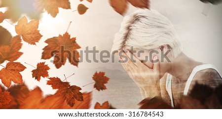 Sad blonde woman crying with head on hands against autumn leaves