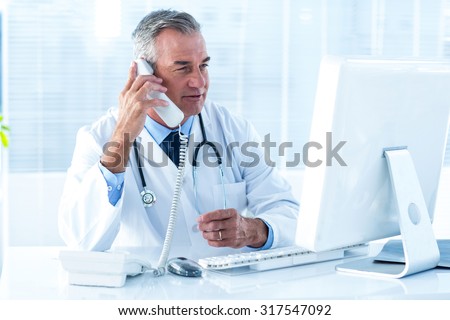 Male doctor in conversation through telephone while looking at computer in hospital