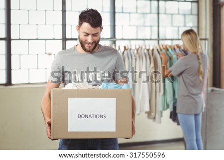 Man holding clothes donation box with woman seen in background at office