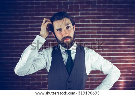 Portrait of man scratching head against brick wall