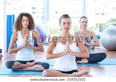 Focused women in lotus pose with praying hands in fitness studio