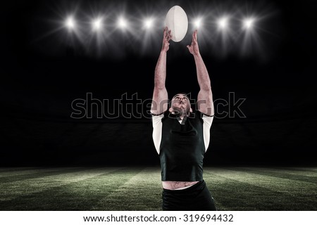 Rugby player catching the ball against football pitch at night with ball and lights