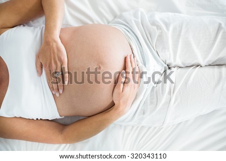 Midsection of pregnant woman holding belly on bed