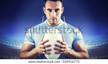 Rugby player looking at camera with ball against rugby stadium
