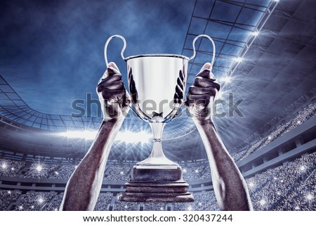 Cropped hand of athlete holding trophy against football stadium