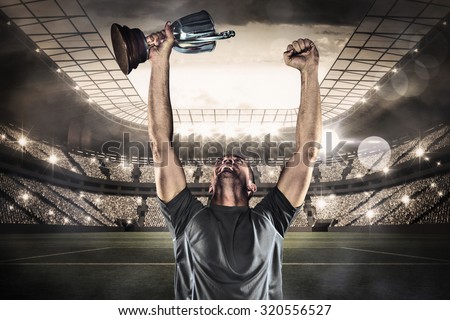 Happy rugby player holding trophy against large football stadium with lights